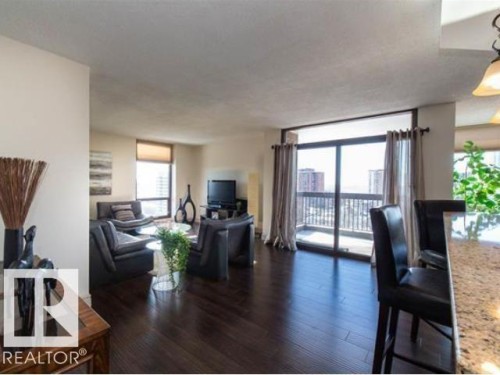 Expansive living area featuring rich, dark wood-finish flooring, a full-height glass balcony door, and a generously sized balcony with metal railings - #1203 10025 113 St Nw, Edmonton, AB - Indoor Photo Showing Living Room