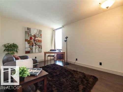 Spacious room featuring wood-finish flooring, light-toned walls, and a large window with vertical blinds - #1203 10025 113 St Nw, Edmonton, AB - Indoor