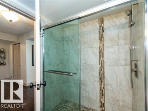 Glass-enclosed shower with a built-in bench, featuring a tiled accent strip and a handheld shower fixture - #1203 10025 113 St Nw, Edmonton, AB - Indoor Photo Showing Bathroom