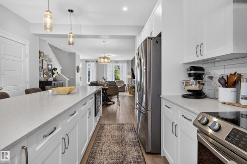 Gourmet kitchen featuring a large island with integrated microwave, white shaker cabinetry with brushed nickel hardware, light-toned countertops, subway tile backsplash, and stainless steel appliances - 6 Daniel Street, Fort Saskatchewan, AB - Indoor Photo Showing Kitchen With Upgraded Kitchen