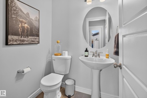 Elegant powder room featuring a pedestal sink with chrome fixtures, a round mirror with integrated lighting, and white subway tile wainscoting - 6 Daniel Street, Fort Saskatchewan, AB - Indoor Photo Showing Bathroom