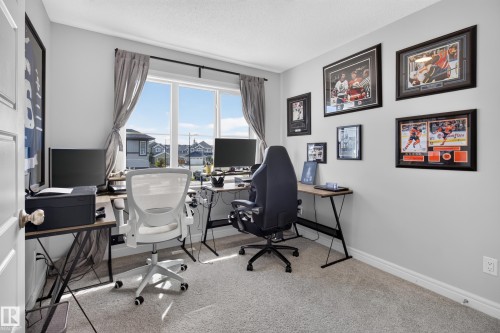Dedicated home office featuring expansive windows with natural light, dual workstations with ergonomic seating, framed sports memorabilia displays, neutral carpeting, and ample desk space ideal for remote work or creative pursuits - 6 Daniel Street, Fort Saskatchewan, AB - Indoor Photo Showing Office