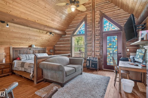Vaulted wood-paneled ceiling with a ceiling fan, log walls, wood-finish flooring, and a door with stained glass accents - 107 Idlehours Drive, Rural Barrhead County, AB - Indoor Photo Showing Bedroom