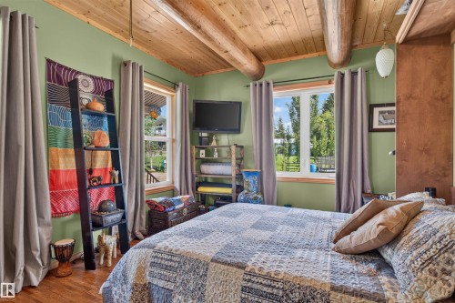 Bedroom featuring a wood-planked ceiling with exposed log beams, two windows with exterior views, wood-finish flooring, and painted green walls - 107 Idlehours Drive, Rural Barrhead County, AB - Indoor Photo Showing Bedroom