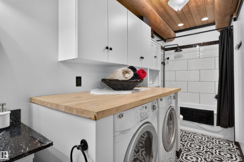Compact bathroom featuring a white subway tile shower, black and white patterned floor tiles, a natural wood countertop, and white overhead cabinetry - 107 Idlehours Drive, Rural Barrhead County, AB - Indoor Photo Showing Laundry Room
