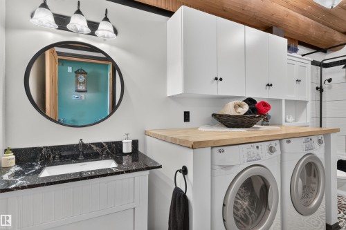 Integrated laundry area featuring stacked appliances beneath a wood-finish countertop - 107 Idlehours Drive, Rural Barrhead County, AB - Indoor Photo Showing Laundry Room
