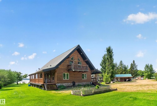 Log cabin exterior featuring a metal roof, stone foundation, and a wrap-around porch - 107 Idlehours Drive, Rural Barrhead County, AB - Outdoor