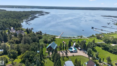 Waterfront property featuring a prominent log-sided residence with a green metal roof, a detached garage, and a private dock extending into the lake - 107 Idlehours Drive, Rural Barrhead County, AB - Outdoor With Body Of Water With View