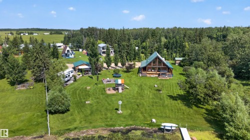A-frame architecture featuring natural wood siding, a green metal roof, a full-length lower deck, and extensive fenestration - 107 Idlehours Drive, Rural Barrhead County, AB - Outdoor With View