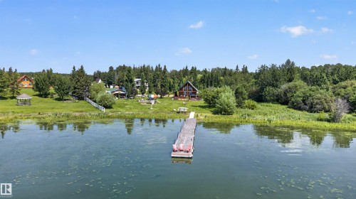 Waterfront property featuring a private dock, A-frame residence, expansive lawn, and mature trees - 107 Idlehours Drive, Rural Barrhead County, AB - Outdoor With Body Of Water With View