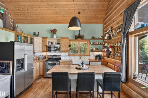 Kitchen featuring wood-finish flooring, wood cabinetry, stainless steel appliances, a white subway tile backsplash, and a large wood-top island with seating - 107 Idlehours Drive, Rural Barrhead County, AB - Indoor