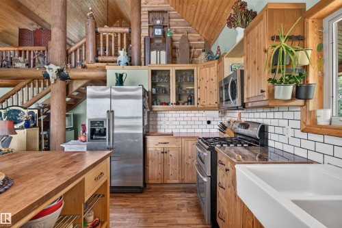 Kitchen featuring a farmhouse sink, stainless steel appliances, wood-finish flooring, white subway tile backsplash, and knotty pine cabinetry - 107 Idlehours Drive, Rural Barrhead County, AB - Indoor Photo Showing Kitchen