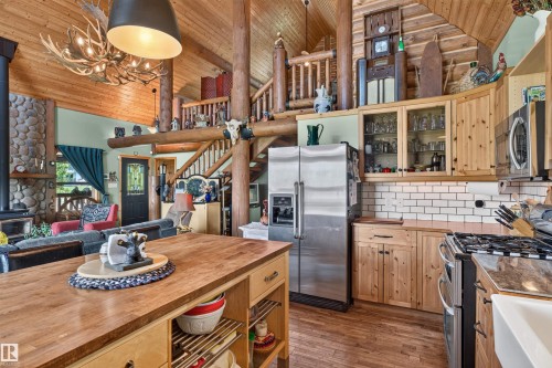 Open-concept kitchen featuring wood-finish flooring, natural wood cabinetry, subway tile backsplash, and a large central island with butcher block countertop - 107 Idlehours Drive, Rural Barrhead County, AB - Indoor Photo Showing Kitchen