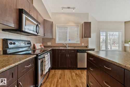 Kitchen featuring dark wood-finish cabinetry, stainless steel appliances, speckled countertops, and wood-finish flooring - #120 8931 156 St Nw, Edmonton, AB - Indoor Photo Showing Kitchen With Stainless Steel Kitchen