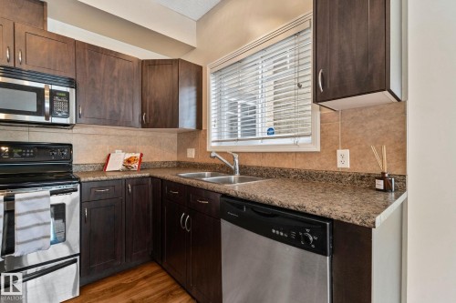 Modern kitchen featuring dark cabinetry with stainless steel hardware, granite countertops, and a coordinating backsplash - #120 8931 156 St Nw, Edmonton, AB - Indoor Photo Showing Kitchen With Double Sink