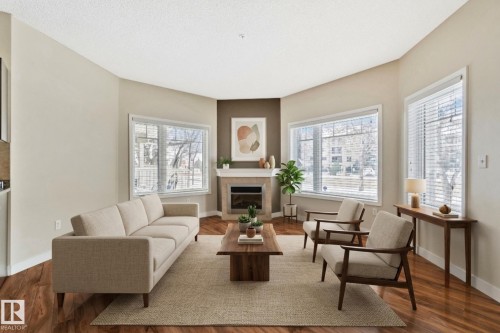 Living area featuring wood-finish flooring and a corner fireplace with a mantel - #120 8931 156 St Nw, Edmonton, AB - Indoor Photo Showing Living Room With Fireplace