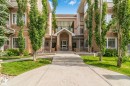 Building exterior featuring a stucco facade, multiple windows, a prominent arched entrance, and established landscaping with trees and grass - #120 8931 156 St Nw, Edmonton, AB 