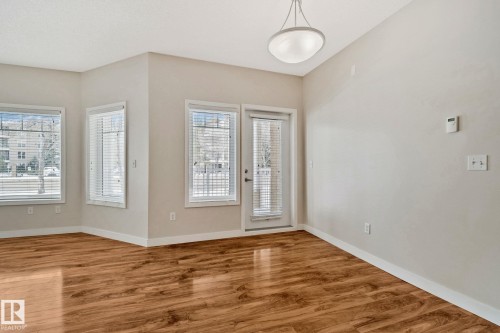 Bright corner room showcasing gleaming wood-finish flooring, abundant natural light from multiple windows with plantation shutters, and neutral wall finishes - #120 8931 156 St Nw, Edmonton, AB - Indoor Photo Showing Other Room