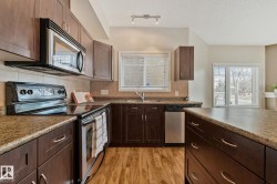 Kitchen featuring dark wood-finish cabinetry, stainless steel appliances, speckled countertops, and wood-finish flooring - 