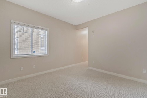 Bright secondary bedroom featuring neutral wall finishes, neutral carpet flooring, and abundant natural light from a large window with plantation shutters - #120 8931 156 St Nw, Edmonton, AB - Indoor Photo Showing Other Room