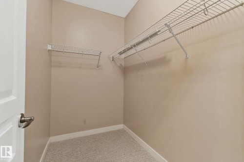 Walk-in closet featuring wire shelving, wall-mounted hanging rods, light-toned carpeting, and a white trim baseboard - #120 8931 156 St Nw, Edmonton, AB - Indoor With Storage