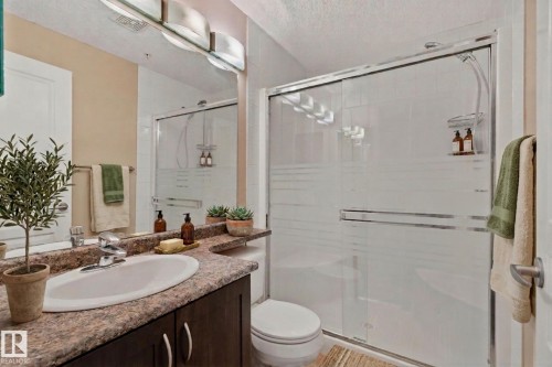 Bathroom featuring a dark wood-finish vanity with an integrated sink, patterned countertop, and a mirrored wall - #120 8931 156 St Nw, Edmonton, AB - Indoor Photo Showing Bathroom