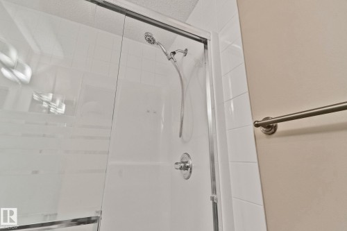 Shower enclosure with clear glass doors, white tiled walls, a brushed nickel showerhead, and a coordinating single-handle control - #120 8931 156 St Nw, Edmonton, AB - Indoor Photo Showing Bathroom