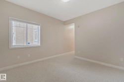 Bright secondary bedroom featuring neutral wall finishes, neutral carpet flooring, and abundant natural light from a large window with plantation shutters - 