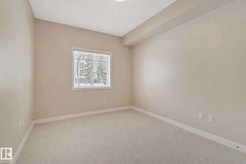 Bright bedroom showcasing neutral wall finishes, plush carpet flooring, and abundant natural light from a large window - #120 8931 156 St Nw, Edmonton, AB - Indoor Photo Showing Other Room