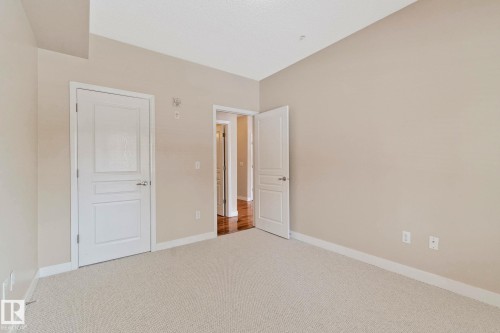 Neutral-toned room featuring a light-colored carpet, white trim, and two paneled doors - #120 8931 156 St Nw, Edmonton, AB - Indoor Photo Showing Other Room