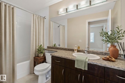 Bathroom featuring a bathtub with shower, a vanity with an integrated sink, dark wood-finish cabinetry, a large mirror, and overhead strip lighting - #120 8931 156 St Nw, Edmonton, AB - Indoor Photo Showing Bathroom