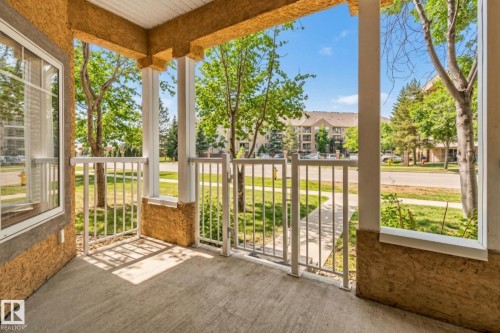 Covered front patio featuring a textured stucco exterior, white metal railings, a concrete floor, and a large window - #120 8931 156 St Nw, Edmonton, AB - Outdoor With Deck Patio Veranda With Exterior