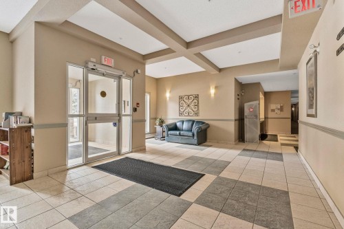 Welcoming lobby entry featuring a coffered ceiling with skylights, polished tile flooring in neutral tones, and glass entry doors with brushed metal hardware - #120 8931 156 St Nw, Edmonton, AB - Indoor Photo Showing Other Room