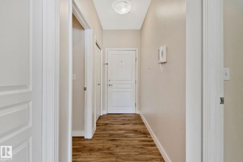 Bright hallway featuring warm wood-finish flooring, clean white trim work, and multiple white panel doors with polished hardware - #120 8931 156 St Nw, Edmonton, AB - Indoor Photo Showing Other Room