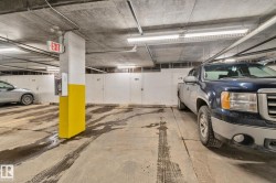 Underground parking space featuring a concrete floor and ceiling, fluorescent lighting, an exit sign, and individual storage units - 