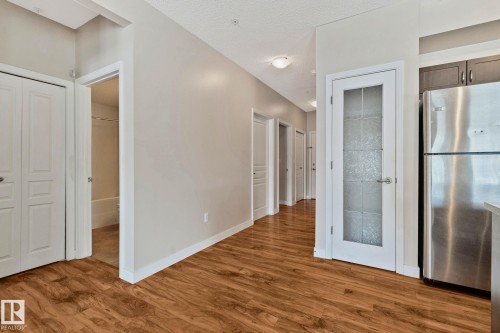 Spacious hallway featuring warm wood-finish flooring, clean white trim throughout, and multiple white panel doors - #120 8931 156 St Nw, Edmonton, AB - Indoor
