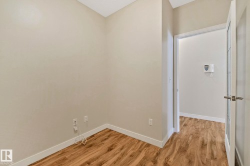 Neutral wall paint, wood-finish flooring, white baseboards, and a paneled interior door with a brushed nickel handle - #120 8931 156 St Nw, Edmonton, AB - Indoor Photo Showing Other Room
