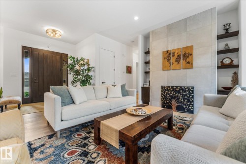 Spacious living area featuring light wood-finish flooring, a contemporary fireplace with light-toned tile surround, and dark wood built-in shelving - #52 Riverstone Close, Rural Sturgeon County, AB - Indoor Photo Showing Living Room
