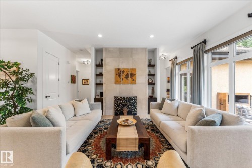 Living area featuring a stone-clad fireplace, integrated shelving, recessed lighting, and large windows with transom panels - #52 Riverstone Close, Rural Sturgeon County, AB - Indoor Photo Showing Living Room