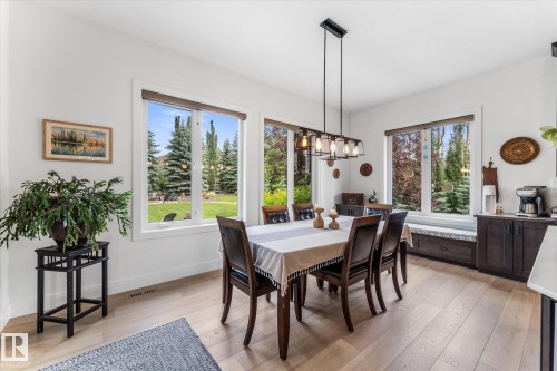 Dining area featuring wood-finish flooring, white walls, and multiple large windows overlooking a landscaped rear yard - #52 Riverstone Close, Rural Sturgeon County, AB - Indoor Photo Showing Dining Room