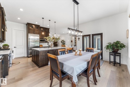 Open-concept dining area featuring light wood-finish flooring, a linear chandelier, and double French doors with dark trim - #52 Riverstone Close, Rural Sturgeon County, AB - Indoor Photo Showing Dining Room