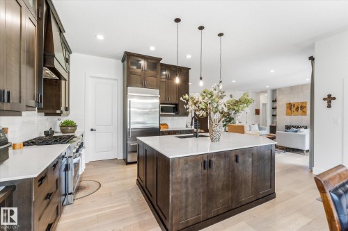 Kitchen featuring a large island with white countertop, dark wood-finish cabinetry, stainless steel appliances, and light wood-finish flooring - #52 Riverstone Close, Rural Sturgeon County, AB - Indoor Photo Showing Kitchen With Upgraded Kitchen