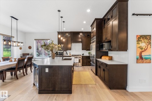 Open-concept kitchen featuring dark wood cabinetry, light wood-finish flooring, and a large central island with a built-in beverage cooler - #52 Riverstone Close, Rural Sturgeon County, AB - Indoor