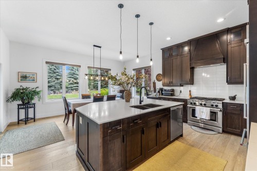 Gourmet kitchen featuring a large island with sink, dark wood cabinetry, stainless steel appliances, and wood-finish flooring - #52 Riverstone Close, Rural Sturgeon County, AB - Indoor Photo Showing Kitchen With Double Sink With Upgraded Kitchen