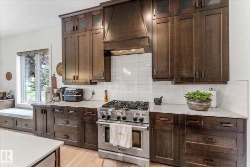 Gourmet kitchen featuring dark wood cabinetry, a professional-grade stainless steel range, white subway tile backsplash, light-toned countertops, and a built-in window seat - #52 Riverstone Close, Rural Sturgeon County, AB - Indoor Photo Showing Kitchen