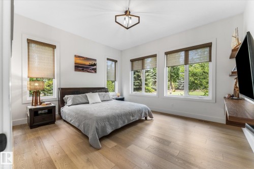 Bright room featuring wood-finish flooring, multiple windows with natural light, a contemporary ceiling fixture, a dark wood-finish headboard, and a built-in floating entertainment console - #52 Riverstone Close, Rural Sturgeon County, AB - Indoor Photo Showing Bedroom