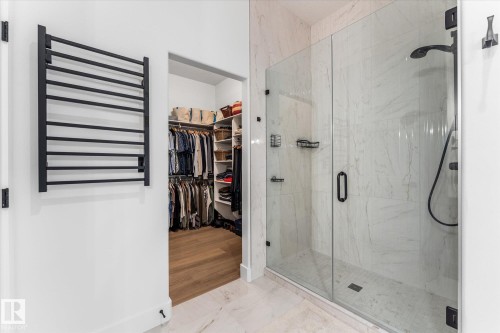 Spacious walk-in closet with built-in shelving, wood-finish flooring, and a glass-enclosed shower featuring white marble-look tiling and matte black fixtures - #52 Riverstone Close, Rural Sturgeon County, AB - Indoor Photo Showing Bathroom