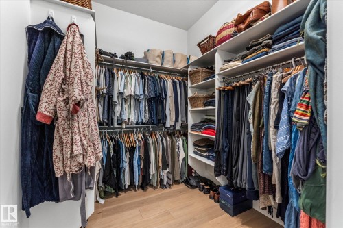 Custom closet system featuring wood-finish flooring, white built-in shelving, and multiple hanging rods for optimized organization - #52 Riverstone Close, Rural Sturgeon County, AB - Indoor With Storage