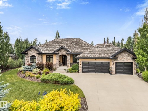 Stone and stucco exterior featuring a multi-gabled roofline with shake shingles, arched windows, and a multi-car garage with black panel doors - #52 Riverstone Close, Rural Sturgeon County, AB - Outdoor With Facade
