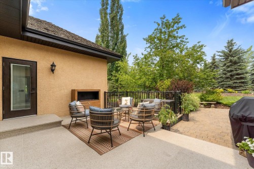 Outdoor patio featuring a stucco exterior, built-in fireplace, black metal railing, and a paver stone area - #52 Riverstone Close, Rural Sturgeon County, AB - Outdoor With Deck Patio Veranda With Exterior